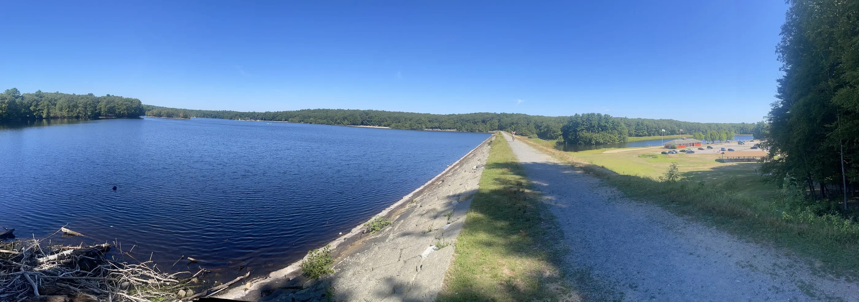 A gravel path along a lake dam under a clear blue sky
